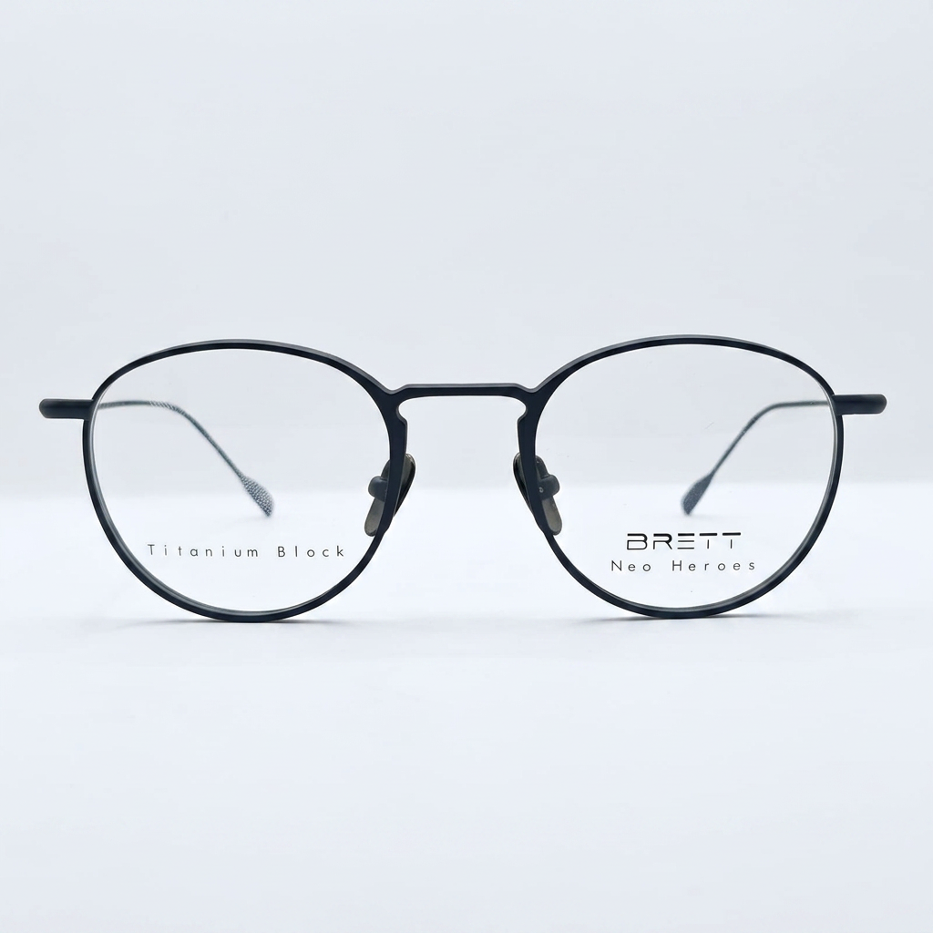 Round black eyeglasses with a metal bridge; left lens shows 'Titanium Block' and right lens shows 'BRETT Neo Heroes' branding.